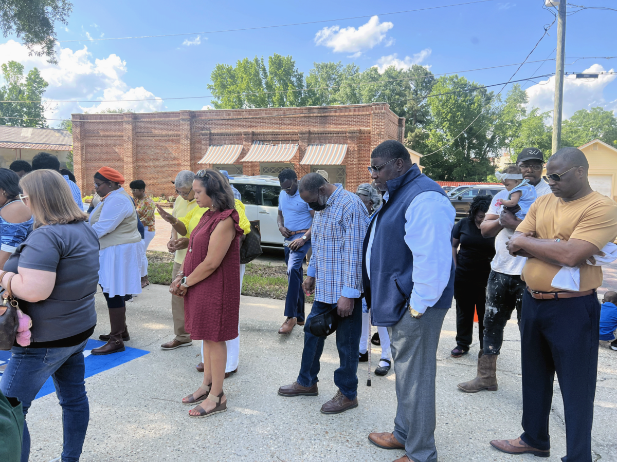 Community members bow their heads in prayer during the Hall Health grand opening ceremony. Supporters gathered outside the downtown Hattiesburg facility to mark the launch of the new clinic.