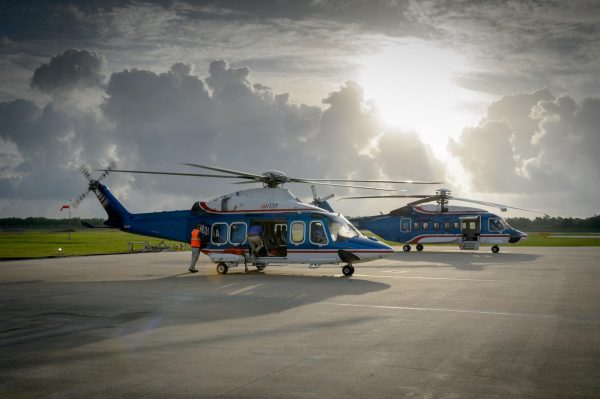 Two blue and white Chevron helicopters sit on a runway at sunrise, with crew members loading gear for offshore transport.