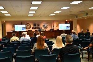 Audience members listen as an MDMR staff member presents slides during a public information session.