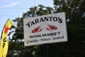 A large outdoor sign for Taranto’s Woolmarket restaurant featuring crawfish illustrations and seafood offerings.