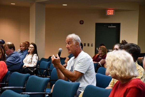 A man in a white shirt holds a microphone while speaking during a seafood labeling Q&A session.