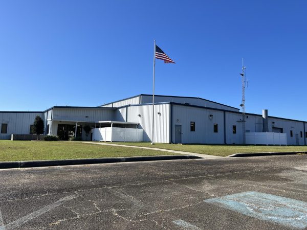 A white metal airport terminal building with an American flag flying outside and a clear blue sky overhead.