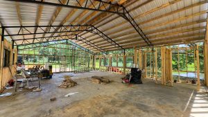 Interior of an unfinished classroom with exposed wooden framing, a metal roof and construction materials scattered on a concrete floor.