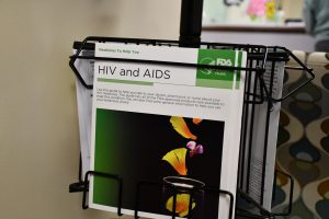 Brochure titled “HIV and AIDS” from the FDA Women’s Health Office displayed in a metal rack inside a health clinic.