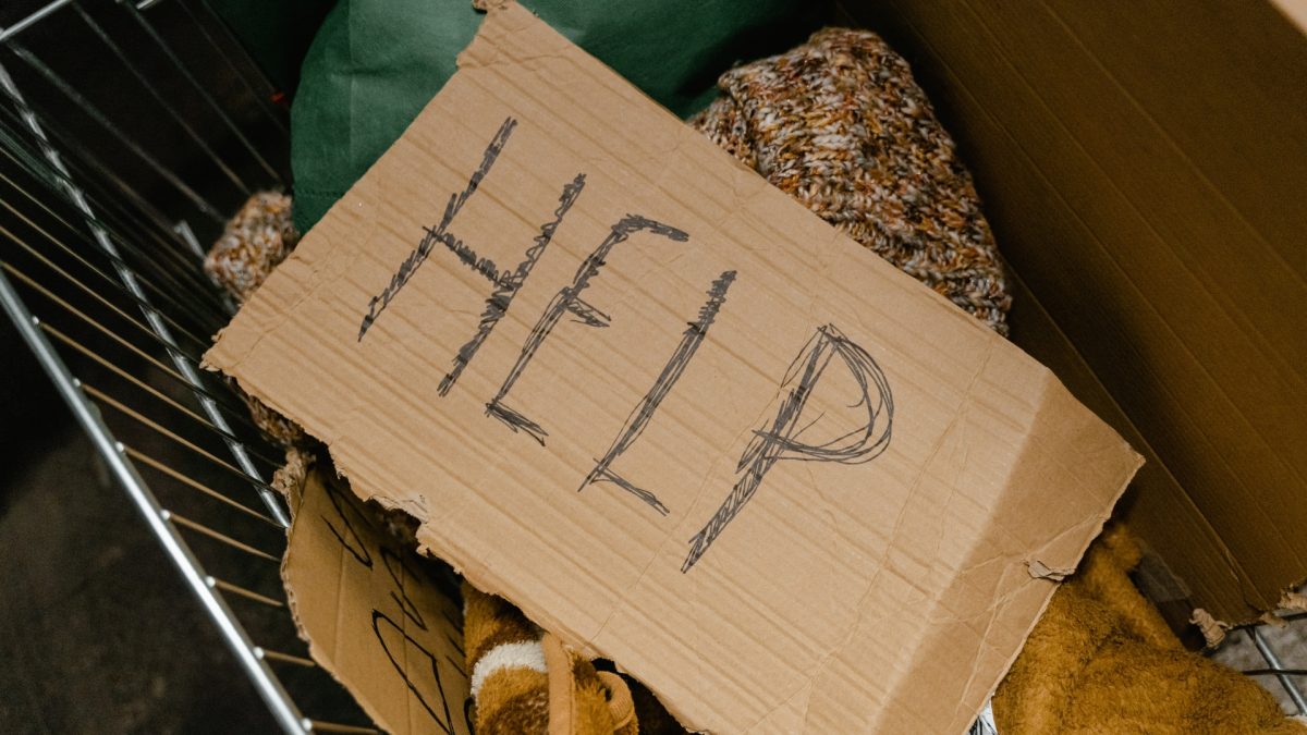 A cardboard sign reading “Help” is placed among blankets and closing in this file photo.