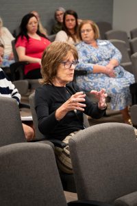 Chancellor Margaret Alfonso speaks at the committee meeting, seated at the front bench next to an American flag.