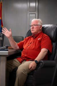 Tim Holleman speaks while seated in the boardroom, raising his hand in discussion.