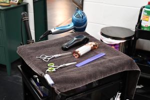 Hair dryer, clippers, scissors and a comb arranged neatly on a stylist’s workstation inside a training facility.