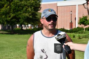 Jordan Davis, a middle school band director wearing sunglasses and a cap, speaks to an RHCJC News reporter during an outdoor interview.