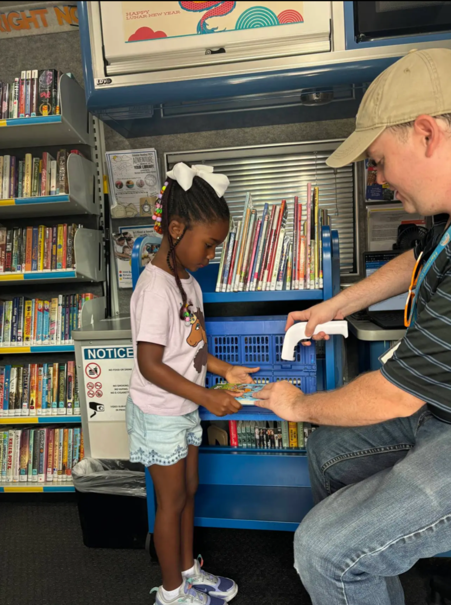 A young girl selects books while Sean Green scans them inside the mobile outreach van filled with children’s books and DVDs.