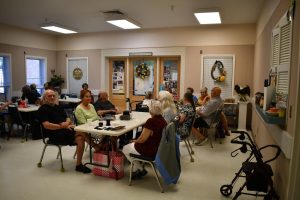 Group of older adults sit around tables in a community room decorated with photos and wreaths.