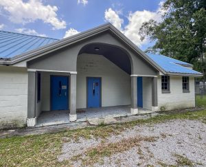 Concrete block building with a sloped blue metal roof and three bright blue doors under a covered entrance.