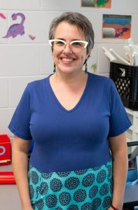 A woman with glasses smiles before a camera.