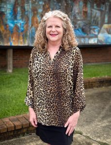 A blonde woman in cheetah print poses before a mural.