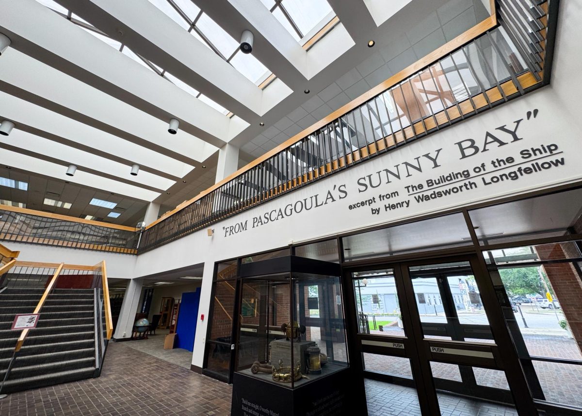 "From Pascagoula's Sunny Bay" is quoted on a wall above glass and black metal doors under a skylight ceiling.