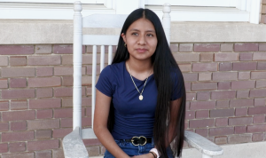 Student sitting in a white rocking chair against a brick wall, looking forward.