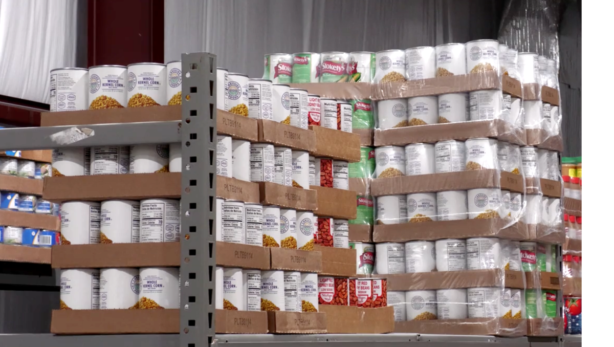 Shelves filled with cases of canned vegetables and beans at a food pantry.
