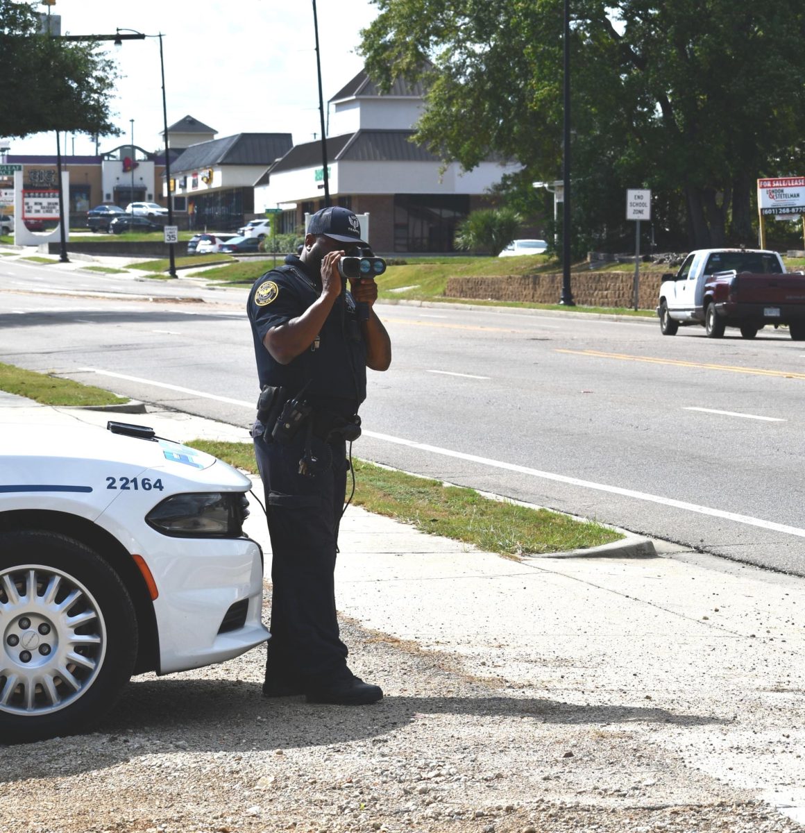 A Hattiesburg Police officer stands on the roadside using a radar gun to check vehicle speeds within city limits.