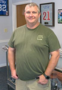 A man in a green shirt smiles and stands inside a local store.