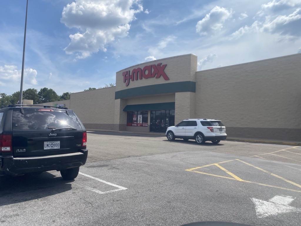 Exterior view of a T.J. Maxx store with cars parked in front under a partly cloudy sky.