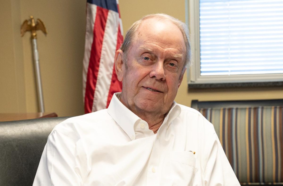 A man in a white shirt speaking while sitting in a chair in an office.
