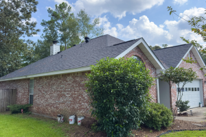 A brick home with a black roof and green shrubbery.