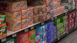 Stacks of soda cartons, including A&W root beer, cream soda, Pepsi and 7UP, lined up on a grocery store shelf.