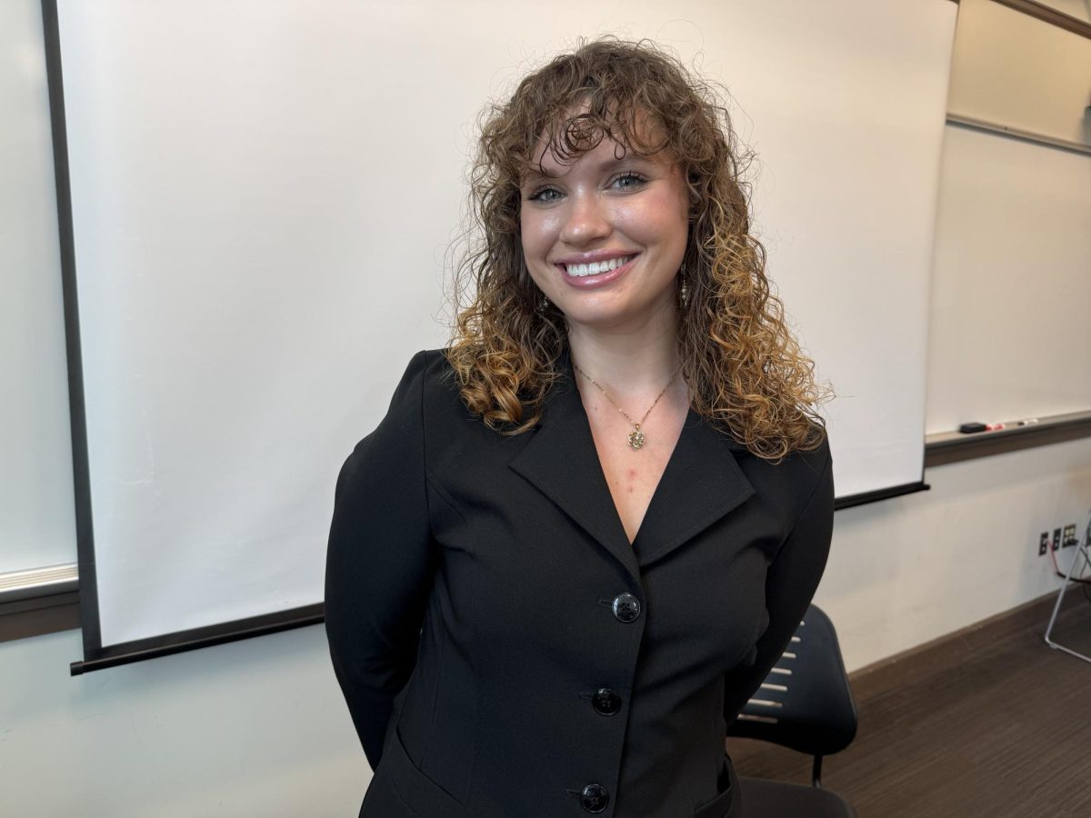 Emma Walker, a University of Southern Mississippi student, smiles while standing in a classroom after discussing the lack of private insurance coverage for hearing aids.