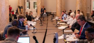 A group of officials sit at a long table and talk.