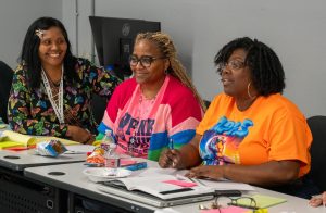 Three teachers seated at a table, discussing materials during a training session.