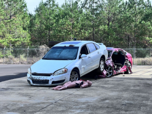 Two damaged vehicles positioned for a mock crash rescue with a training dummy on the ground.