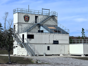Two-story fire training structure made of stacked shipping containers under a blue sky.