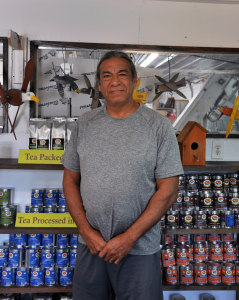 A man in a gray t-shirt and dark gray shorts smiles at the camera, standing in front of product display shelves inside J&D Blueberry Farms shop.