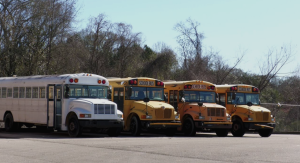 Four school buses, one white and three yellow, parked side by side inside a school bus barn.