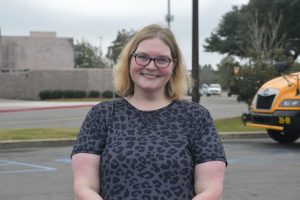 Woman wearing a grey and black leopard print short-sleeve shirt stands in mall parking lot smiling.