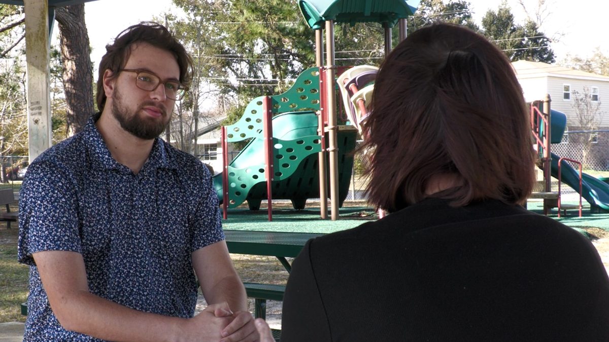 Over the shoulder image of a woman across a picnic table talking to a reporter.