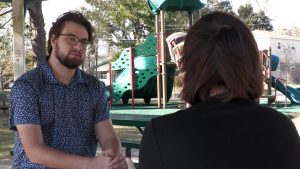 Over the shoulder image of a woman across a picnic table talking to a reporter.