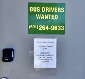 A green and white sign reading “Bus drivers wanted” posted on a building entrance.