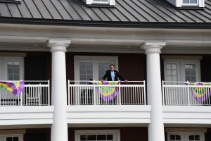A man standing on a balcony with white columns and purple, yellow and green Mardi Gras banners.