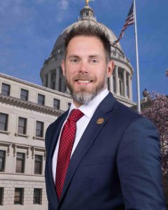 Justin Keen poses in front of the state capitol in a suit and tie.
