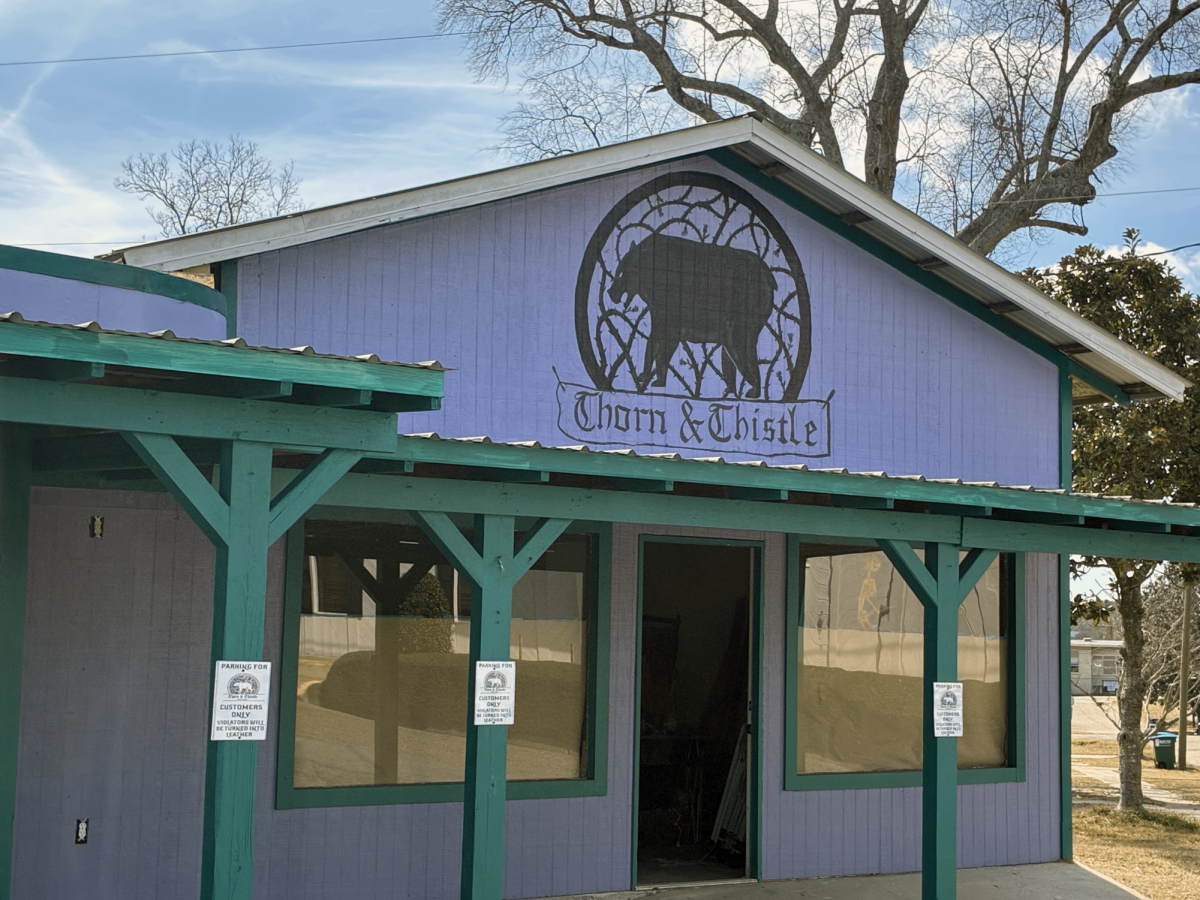 The purple and green exterior of Thorn and Thistle in Lumberton features a sign above the entrance and large front windows.