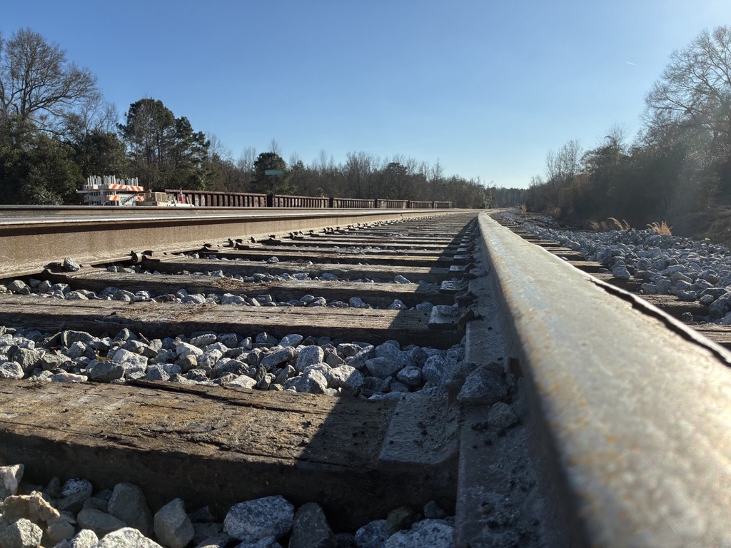 Steel railroad rails and wooden ties run through a rebuilt crossing under a clear sky.