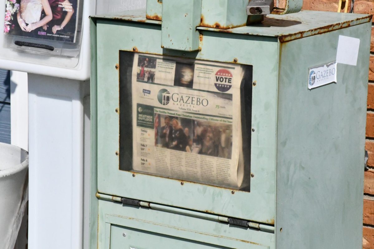 A newspaper sits in a newspaper stand.