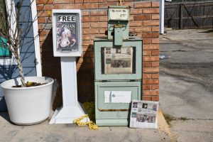 A newspaper stand sits on a sidewalk at the corner of a business.