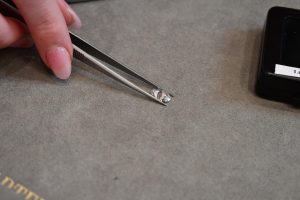 A diamond held with tweezers over a gray display surface.