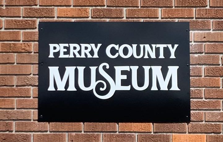 Black sign reading “Perry County Museum” mounted on a red brick wall.