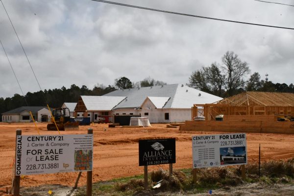 A construction site with buildings at varying levels of completion. Commercial leasing signs line the property in the foreground.