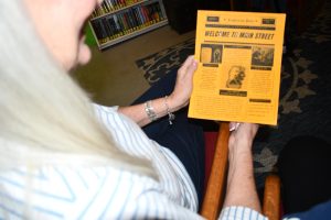 An over-the-shoulder view shows Leanna Dreher holding a copy of the Lumberton Post while seated indoors.