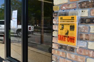 Copies of the Lumberton Post sit in a clear wall-mounted holder labeled “Take One” outside a storefront.
