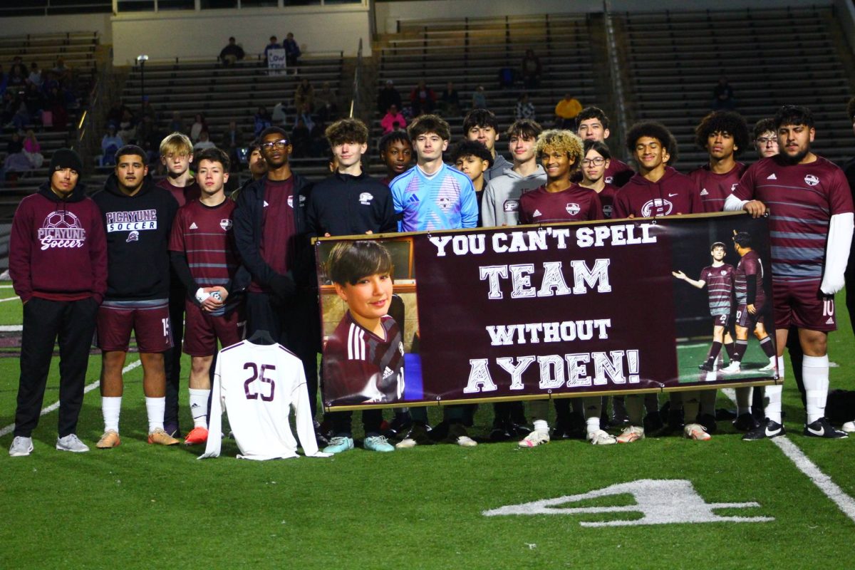 Picayune High School soccer players stand on a field holding Ayden Stockstill’s No. 25 jersey and a memorial banner honoring their teammate.